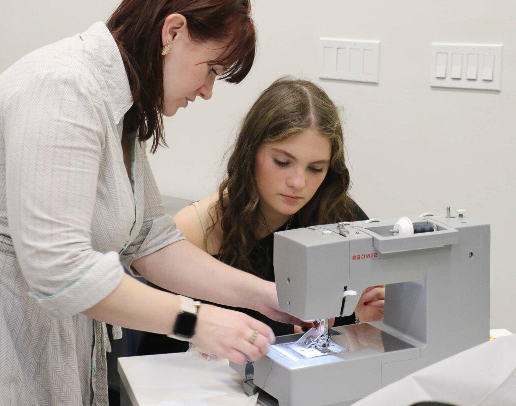 teacher showing student sewing machine technique